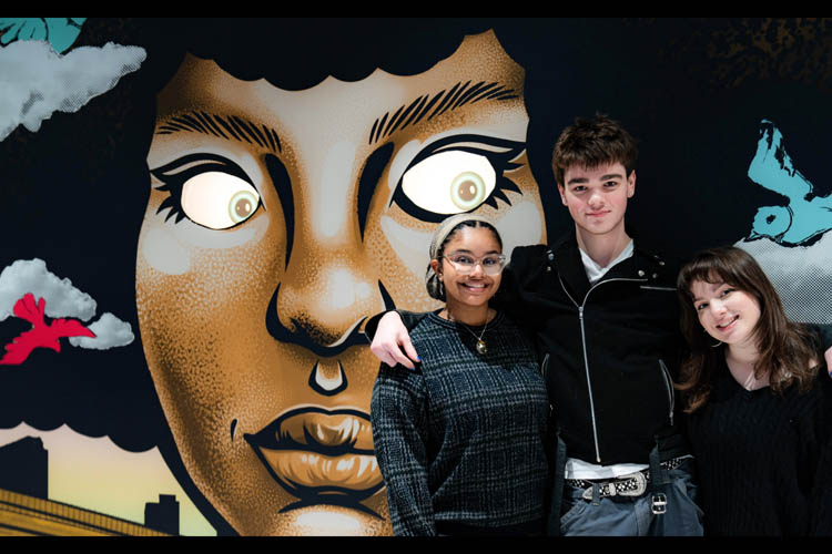 Three people posing in front of a mural of a person.