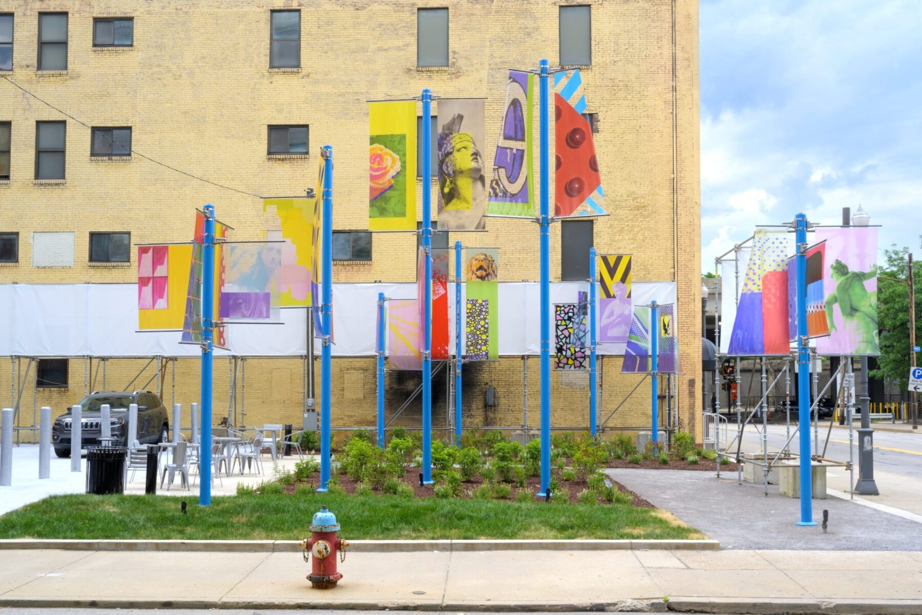 A small park in front of cream building. Blue poles host banners with artwork.